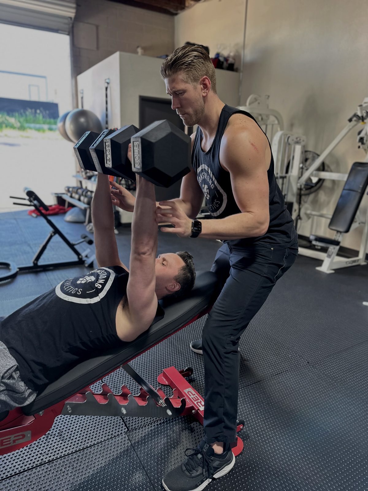 LionStrong coach spotting a client pressing dumbbells on an incline bench